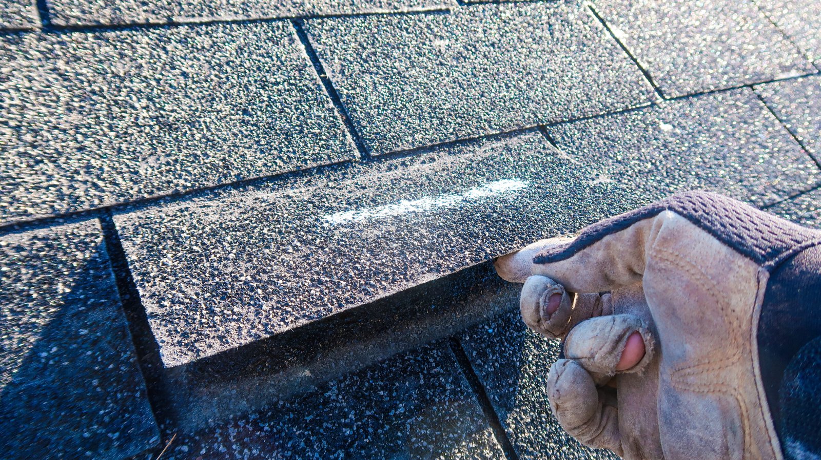 Residential roofer in Durham, inspecting roof shingle on a house roof top after storm damage for leaks.